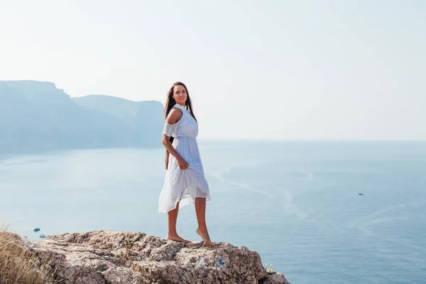 A woman with long hair stands on a rock by the sea — Stock Photo, Image