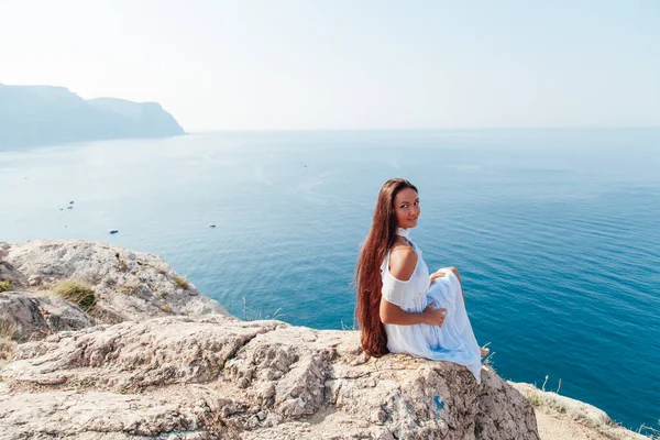 A woman with long hair stands on a rock by the sea — Stock Photo, Image