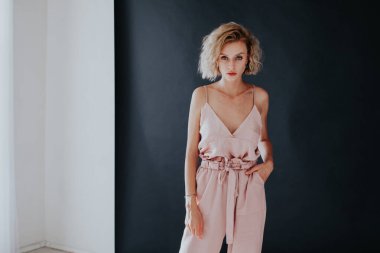 Siyah arka planda pantolon ve bluz giymiş şık bir kadının portresi.