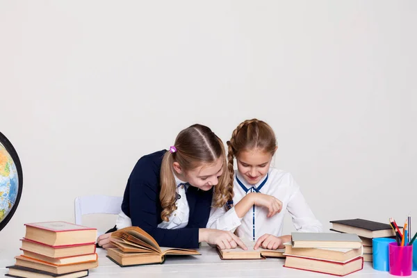 Twee meisjes met boeken en een wereldbol in de klas aan het bureau op school — Stockfoto