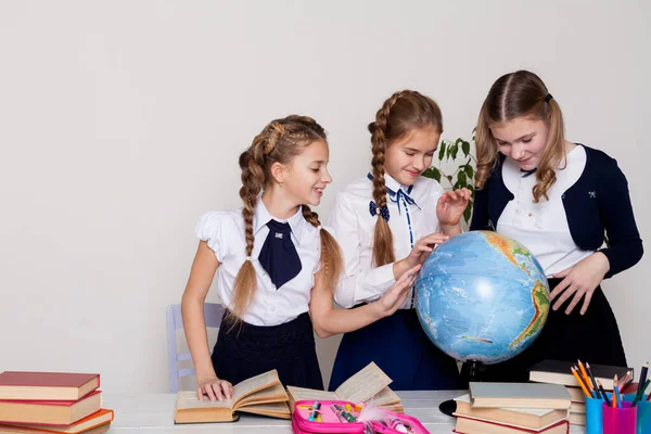 Três meninas com livros e um globo na sala de aula na escola — Fotografia de Stock