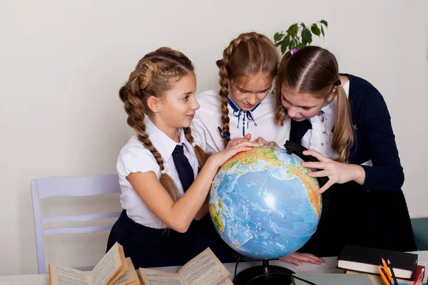 Três meninas com livros e um globo na sala de aula na escola — Fotografia de Stock