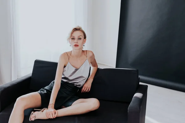 Retrato de una hermosa mujer de moda se sienta en un sofá de oficina negro —  Fotos de Stock