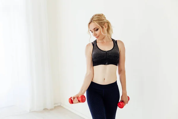 Blonde woman sports in the gym with fitness dumbbells — Stock Photo, Image