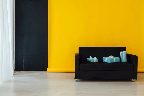 Černá pohovka s dárky v interiéru místnosti se žlutým pozadím — Stock fotografie