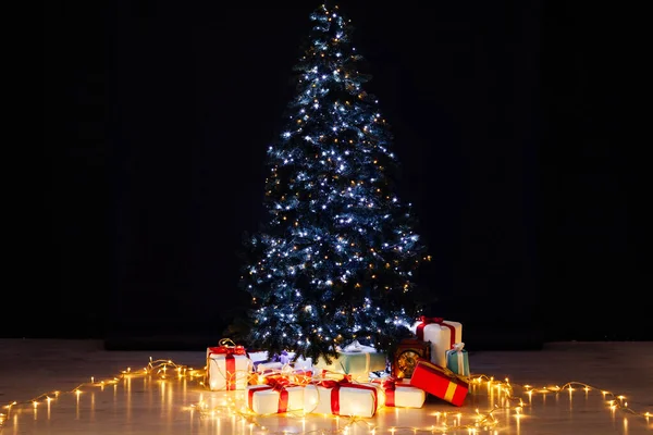 Árbol de Navidad con regalos luces guirnaldas para el nuevo año sobre un fondo negro — Foto de Stock