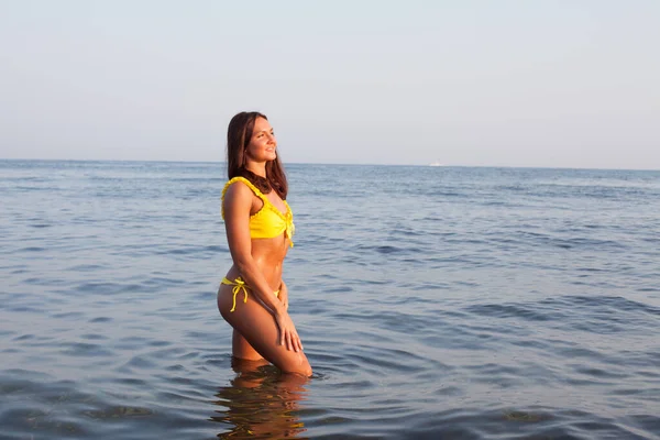 身穿黄色泳衣的美丽的晒黑的女人站在海滩上的海里洗澡 — 图库照片