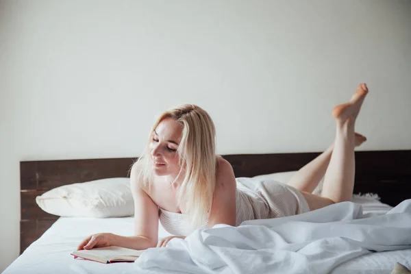 Krásná blondýna žena čte knihu v ložnici v posteli — Stock fotografie