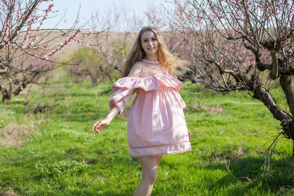 Vacker blond kvinna i rosa klänning promenader runt blommande trädgård — Stockfoto