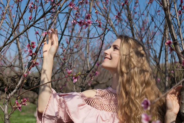 Pembe elbiseli güzel sarışın kadın çiçek açan bahçede yürüyor. — Stok fotoğraf