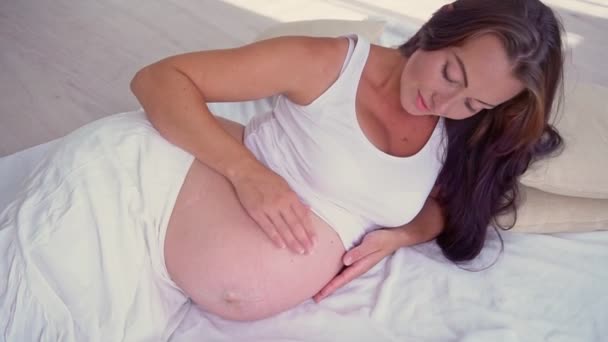 Zwangere vrouw ligt op het bed en streelt een grote buik. — Stockvideo