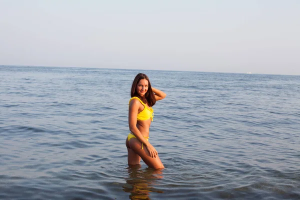 Beautiful woman with long hair in yellow swimsuit sunbathes on the beach — Stock Photo, Image