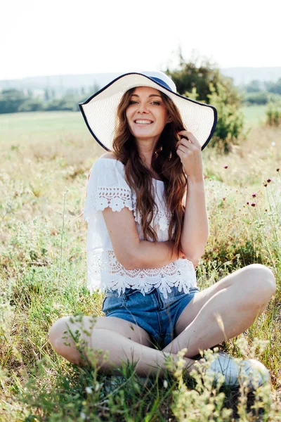 Retrato de uma bela mulher em um chapéu em um campo ao pôr do sol — Fotografia de Stock
