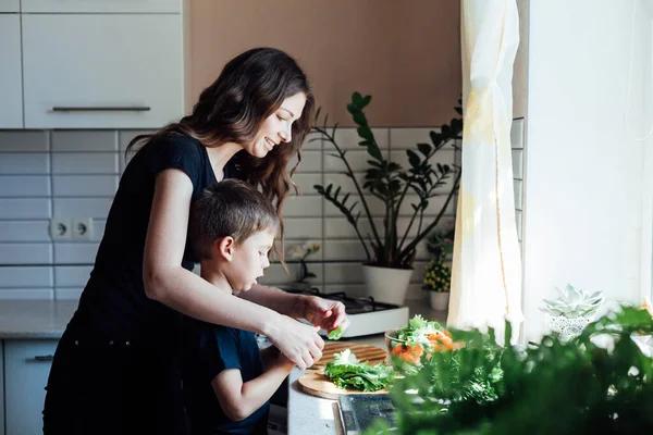 Kleiner Sohn hilft Mutter, Gemüsesalat in der Küche zu kochen — Stockfoto