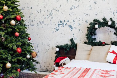 Yatak odasının içinde yeşil bir Noel ağacı yatağı ve yeni yıl dekorasyonu için kırmızı hediyeler var.