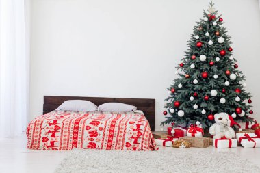 Beyaz yatak odasının içinde mavi Noel ağacı olan bir yatak ve yeni yıl için kırmızı hediyeli kış kartpostalı.
