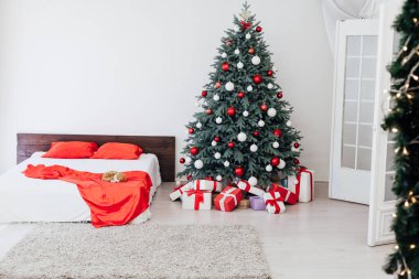 Beyaz yatak odasının içinde mavi Noel ağacı olan bir yatak ve yeni yıl için kırmızı hediyeli kış kartpostalı.