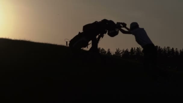 Silhouette de garçon golfeur avec sac de golf au coucher du soleil — Video