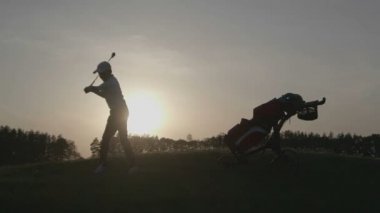 Gün batımında golf çantası ile çocuk golfçü silüeti