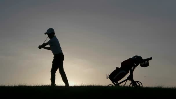 Silhouet van jongen golfer met golftas bij zonsondergang — Stockvideo