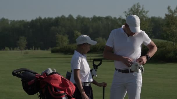 Homme heureux avec son fils golfeurs marchant sur le parcours de golf parfait le jour d'été — Video