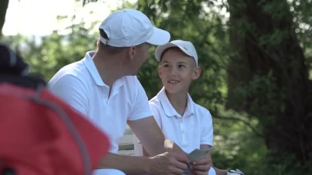 Szczęśliwy człowiek z jego syn golfistów, chodzenie na doskonałe pole golfowe w letni dzień — Wideo stockowe