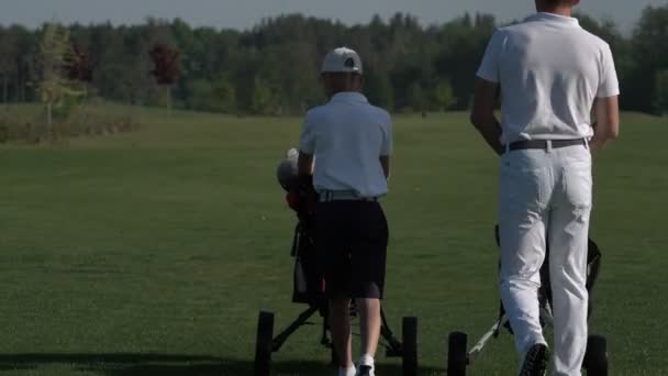 Счастливый мужчина с сыном гуляют по идеальному полю для гольфа в летний день — стоковое видео
