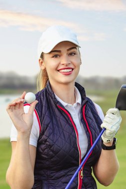 Genç ve güzel bir kadın sonbaharda golf antrenmanı yapıyor.