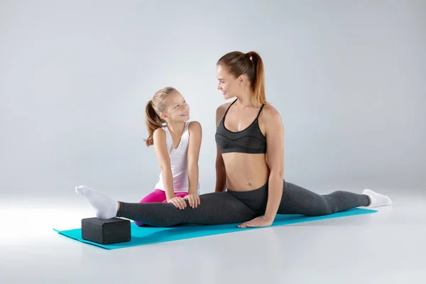 Hermosa mujer y su hija pequeña están haciendo ejercicios en esteras — Foto de Stock