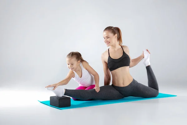 Hermosa mujer y su hija pequeña están haciendo ejercicios en esteras — Foto de Stock