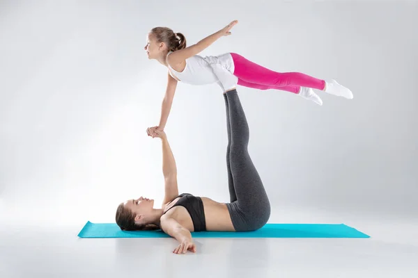 Hermosa mujer y su hija pequeña están haciendo ejercicios en esteras — Foto de Stock