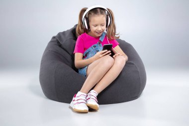 Smartphone kullanarak ve kulaklık ile müzik dinlemek mutlu küçük kız öğrenci