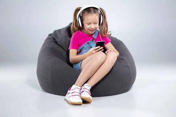 Glad liten skolflicka med smartphone och lyssna på musik med hörlurar — Stockfoto