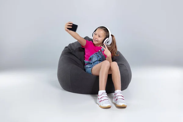 Colegiala feliz utilizando el teléfono inteligente y escuchar música con auriculares — Foto de Stock