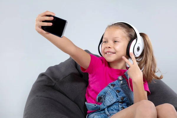 Colegiala feliz utilizando el teléfono inteligente y escuchar música con auriculares — Foto de Stock