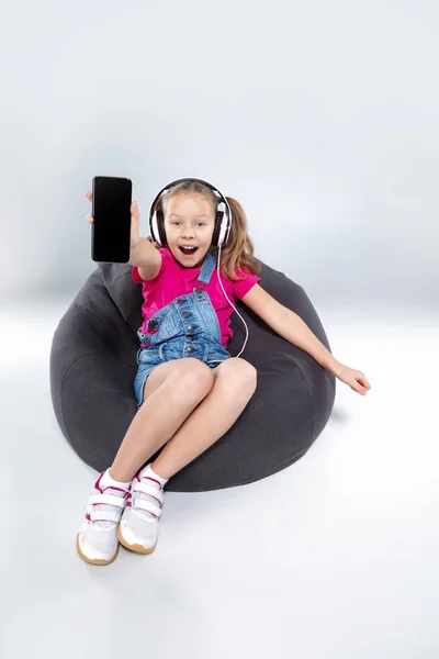 happy little schoolgirl using smartphone with headphones