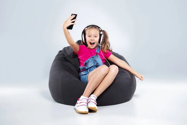 Glad liten skolflicka använda smartphone med hörlurar — Stockfoto