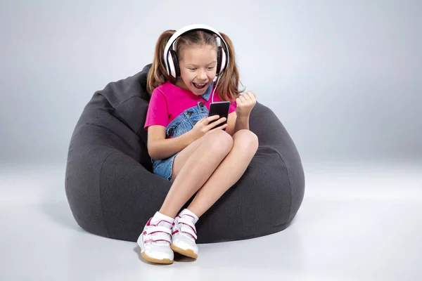 happy little schoolgirl using smartphone with headphones