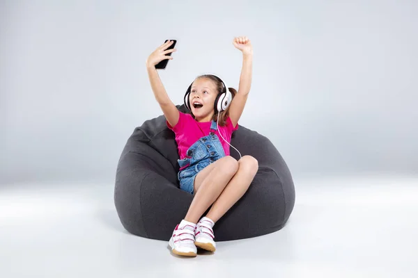 Scolaretta felice utilizzando smartphone con cuffie — Foto Stock