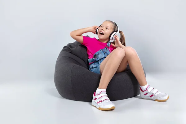 Glad liten skolflicka med smartphone och lyssna på musik med hörlurar — Stockfoto