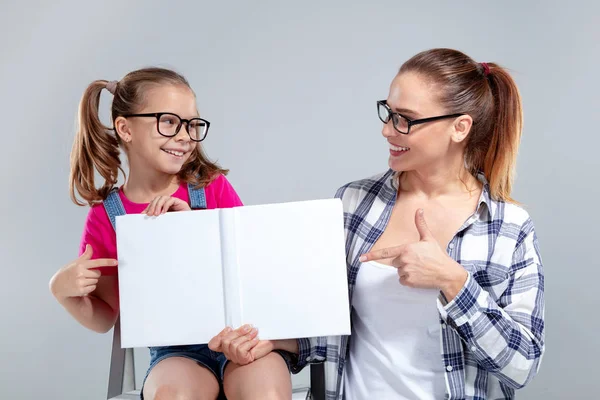 Улыбающаяся красивая женщина и ее дочь в очках с книгой — стоковое фото