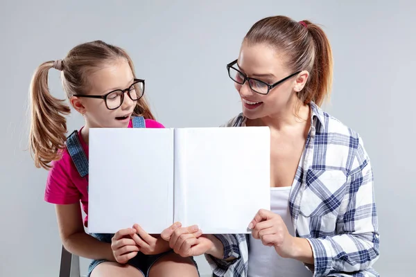 Улыбающаяся красивая женщина и ее дочь в очках с книгой — стоковое фото