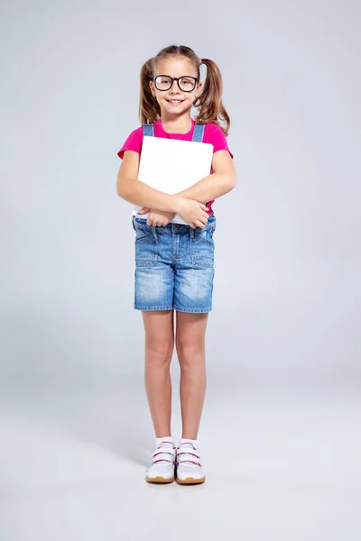 Schoolmeisje in glazen met rugzak en leerboek over de grijze achtergrond — Stockfoto