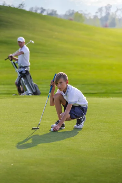 Мальчик играет в гольф, делает выстрел на зеленой — стоковое фото