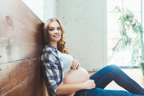 Happy pregnant woman sitting on the floor and touching her belly at home — Stock Photo, Image