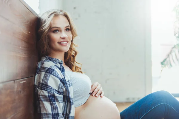 Happy pregnant woman sitting on the floor and touching her belly at home — Stock Photo, Image