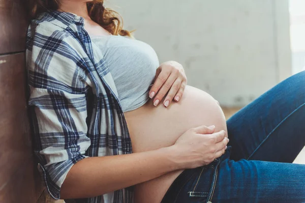 Lycklig gravid kvinna som sitter på golvet och vidrör magen hemma — Stockfoto