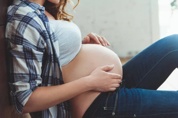 Lycklig gravid kvinna som sitter på golvet och vidrör magen hemma — Stockfoto
