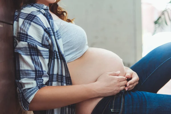 Mujer embarazada feliz sentada en el suelo y tocando su vientre en casa — Foto de Stock