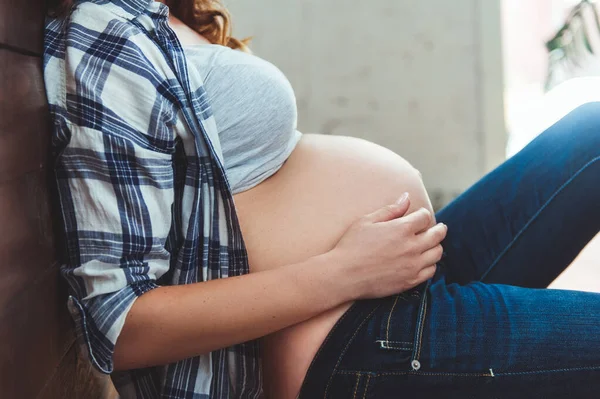 Lycklig gravid kvinna som sitter på golvet och vidrör magen hemma — Stockfoto